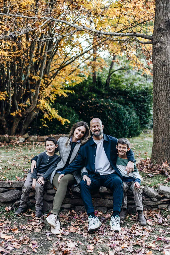 A family of four sits on a stone wall in a lush autumnal garden
