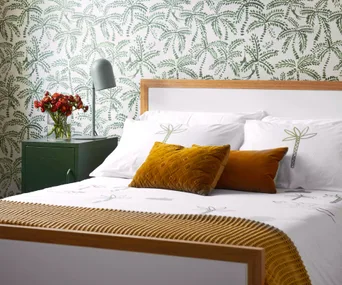 white and timber bed base with white bedding and camel pillows in a green bedroom