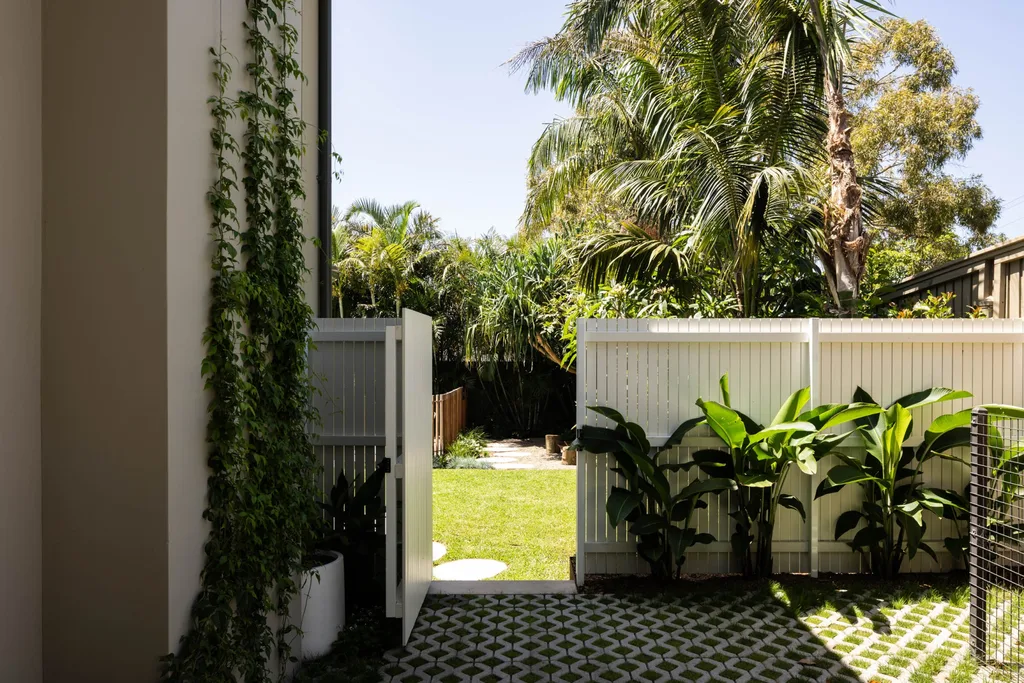 A white fence opening into a tropical-style garden with palm trees