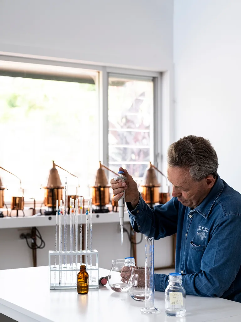 Man in denim shirt at lab bench dropping clear liquid into glass vial with a pipette at Distillery Botanica, Central Coast