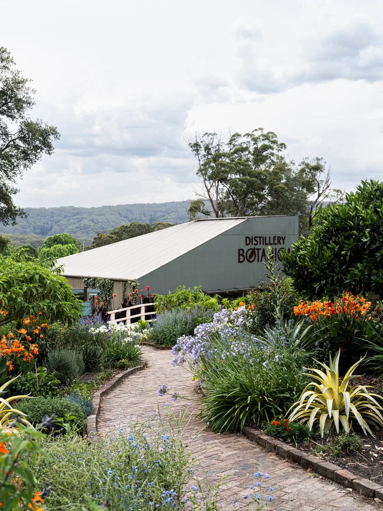 Brick path winding down through bright flower beds to a building with a sign on it saying Distillery Botanica, on the Central Coast