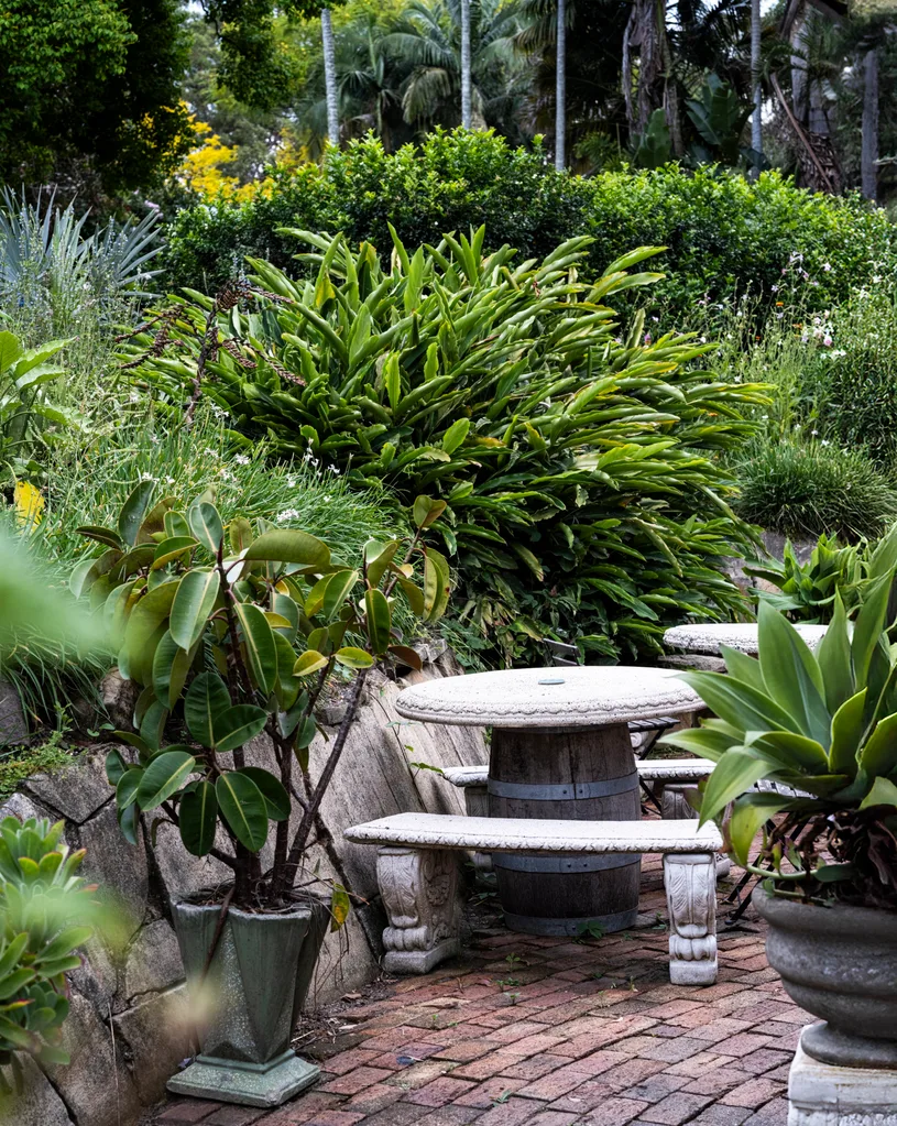 Stone bench and table made of barrel on brick patio in lush garden