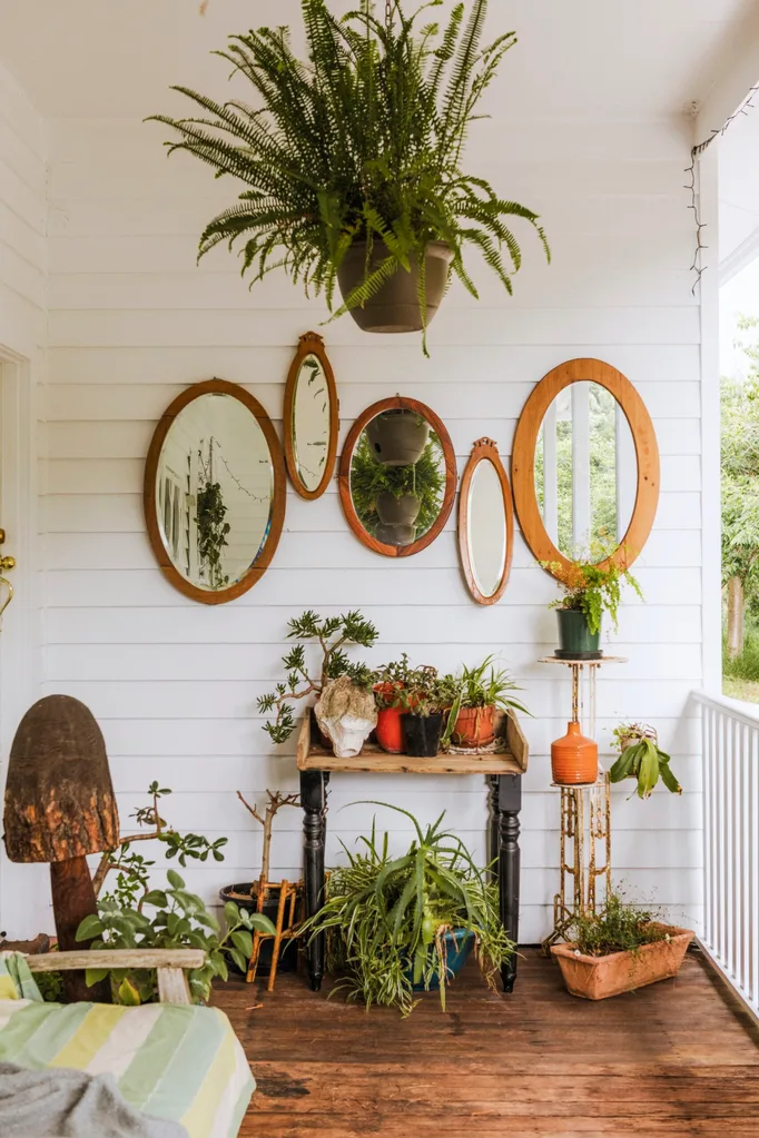 Cvoer verandah on white weatherboard house with mirrors on walls and potted plants in a Grand Ridge House tour