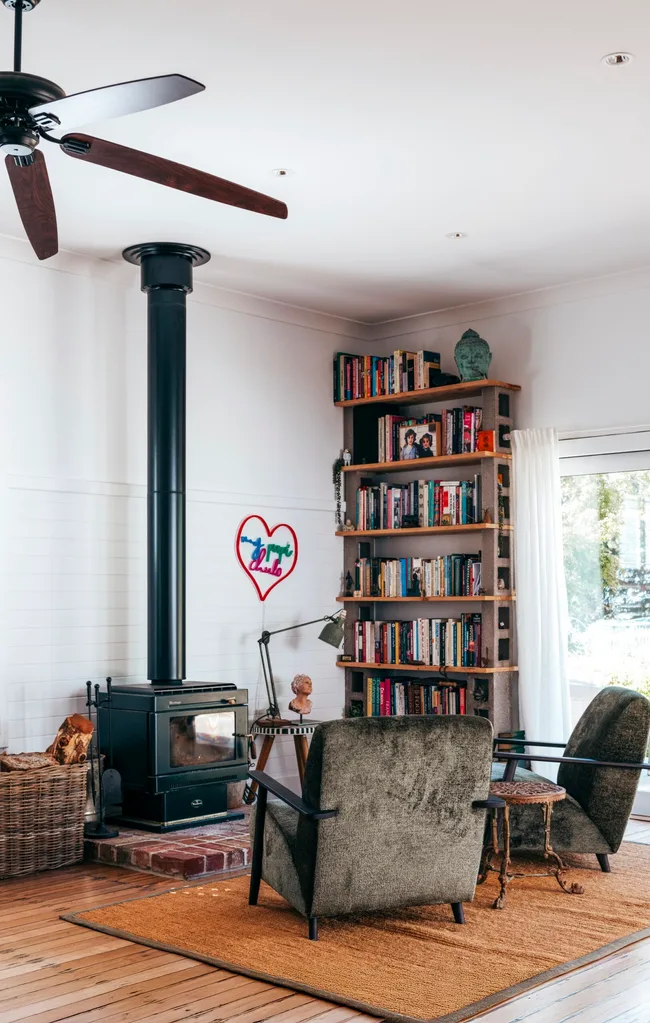 A living room with two grey chairs facing a wood stove with a tall bookshelf in a Grand Ridge House tour