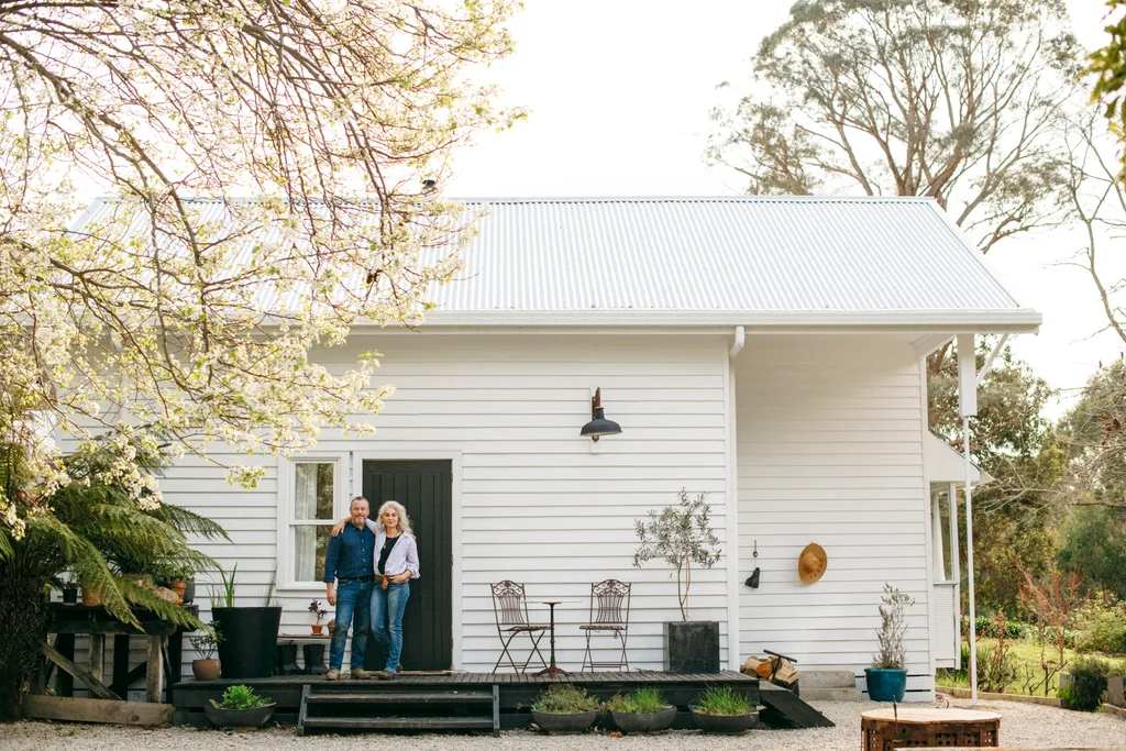Couple outside white weahterboard house with chairs on verandah
