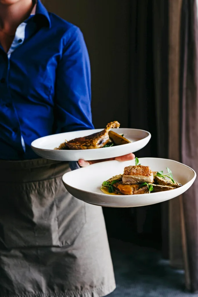 Server holding two large plates filled with beautiful fish dishes