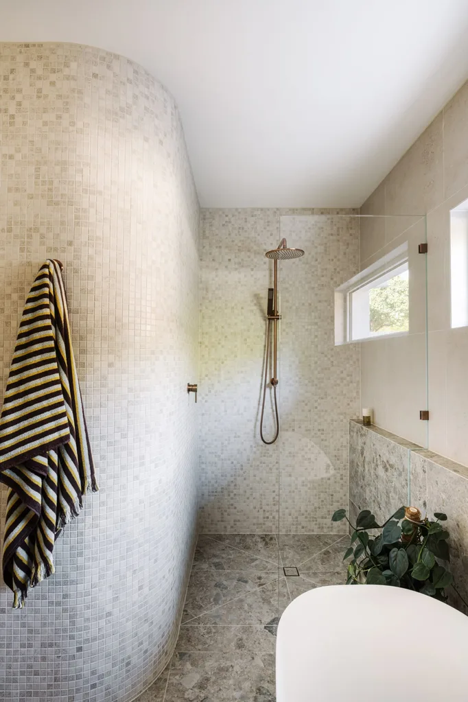 A stone bathroom with mosaic tiling and a freestanding bathtub