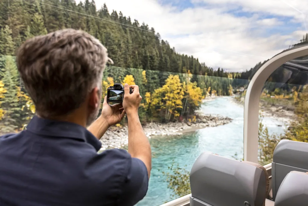 Man taking photos of river through train window in Travel Canada Rocky Mountains
