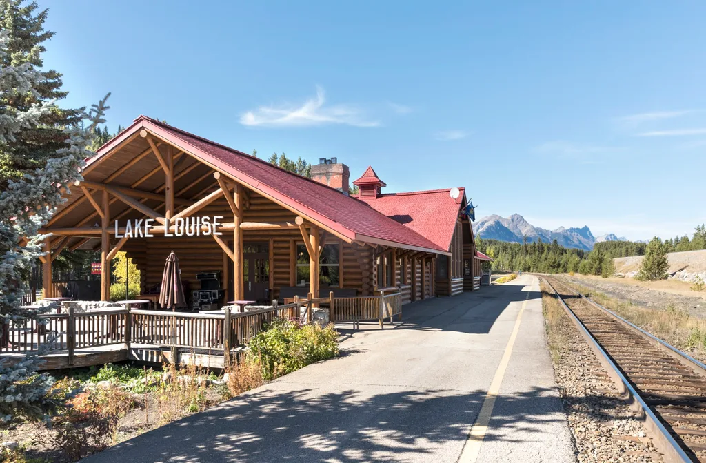 Red-roofed log cabin-style train station with big letters spelling out Lake Louise; mountains in distance in Travel Canada Rocky Mountains