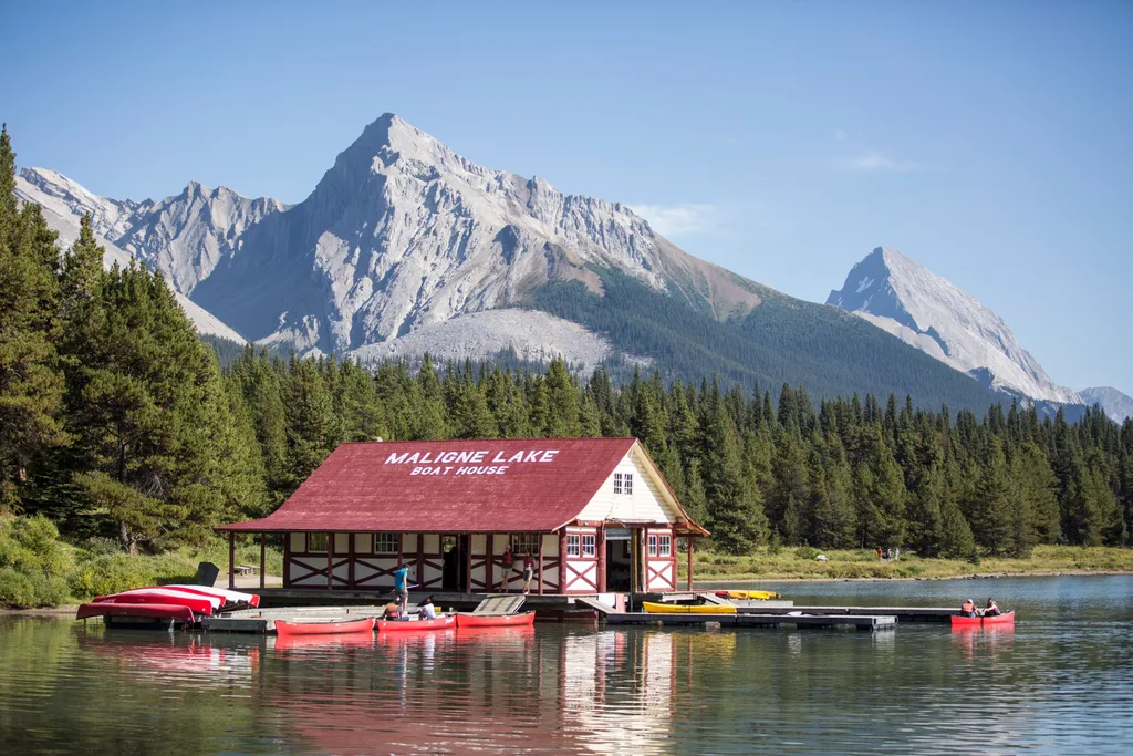 Red-roofed boat house on lake surrounded by fir trees with rocky mountain behind