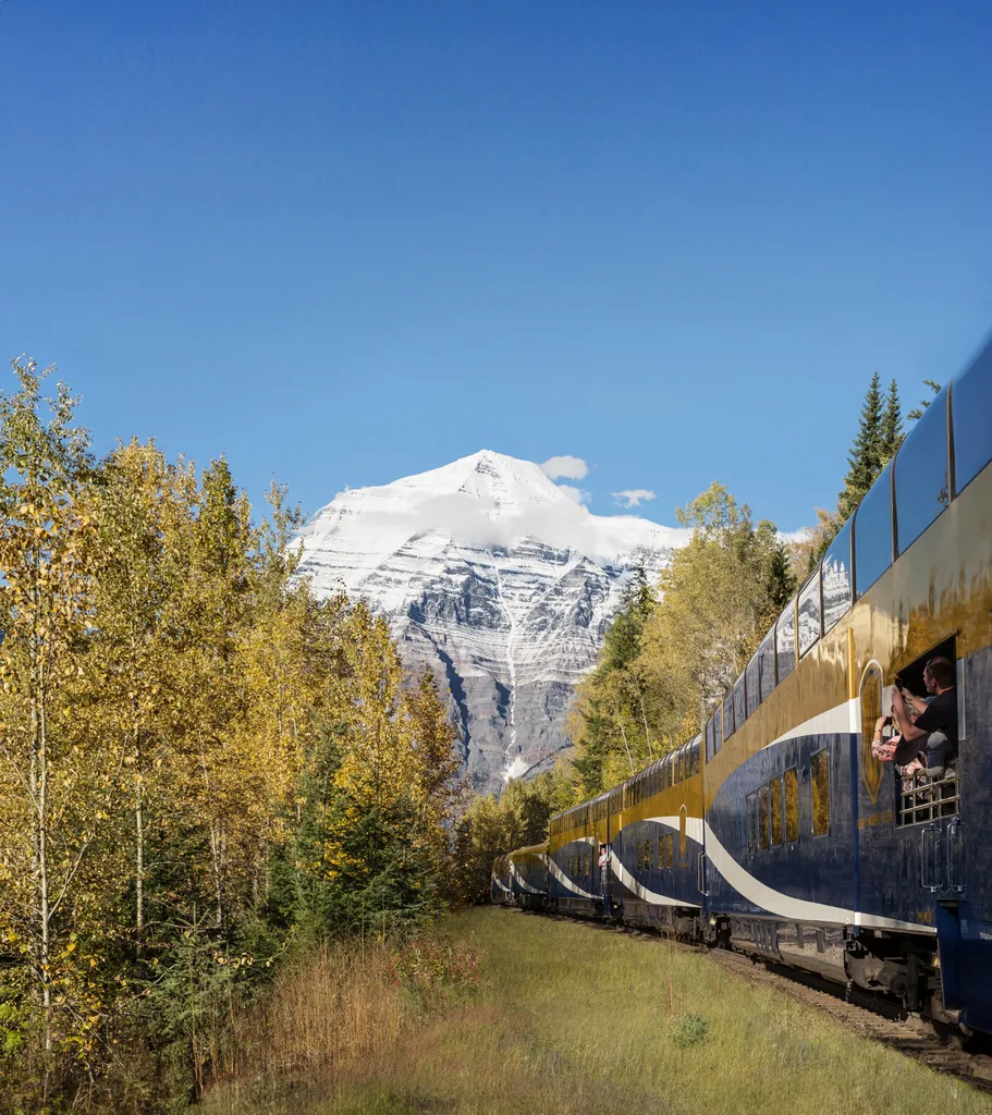 Train running through grassy valley with snow-capped mountains behind in Travel Canada Rocky Mountains