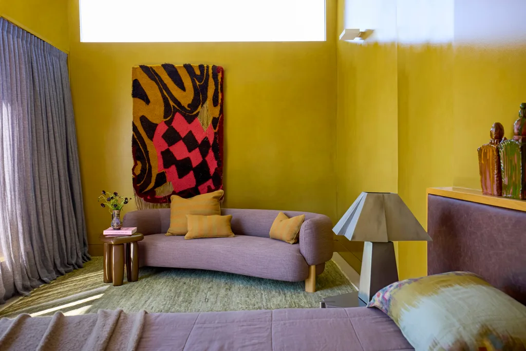 A mustard yellow bedroom with a curved purple lounge and purple curtains