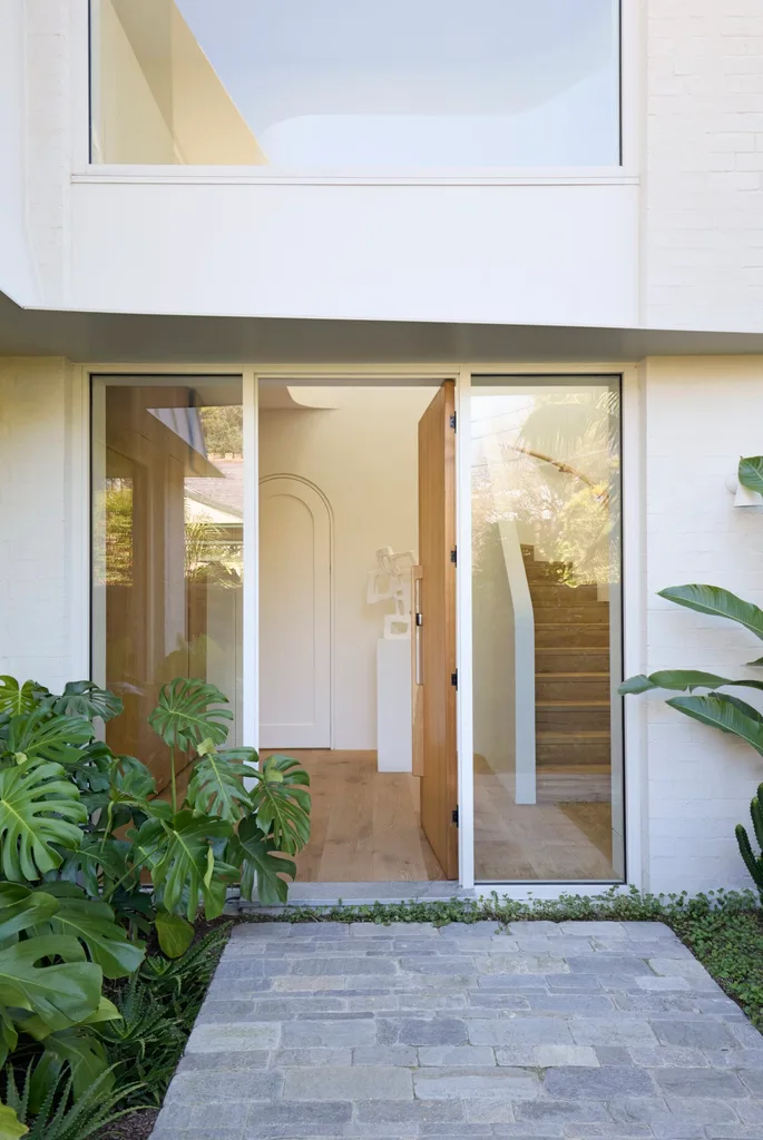 A front entrance lined by monstera plants, leading to an open front door