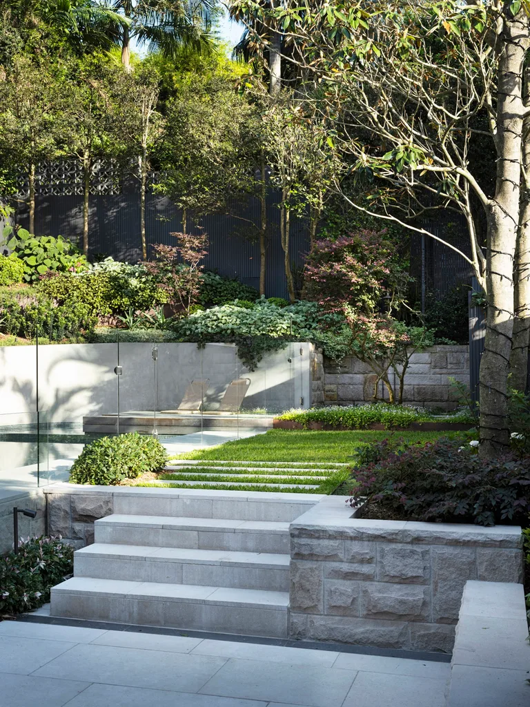 Steps leading up to a swimming pool and small stretch of lawn surrounded by trees