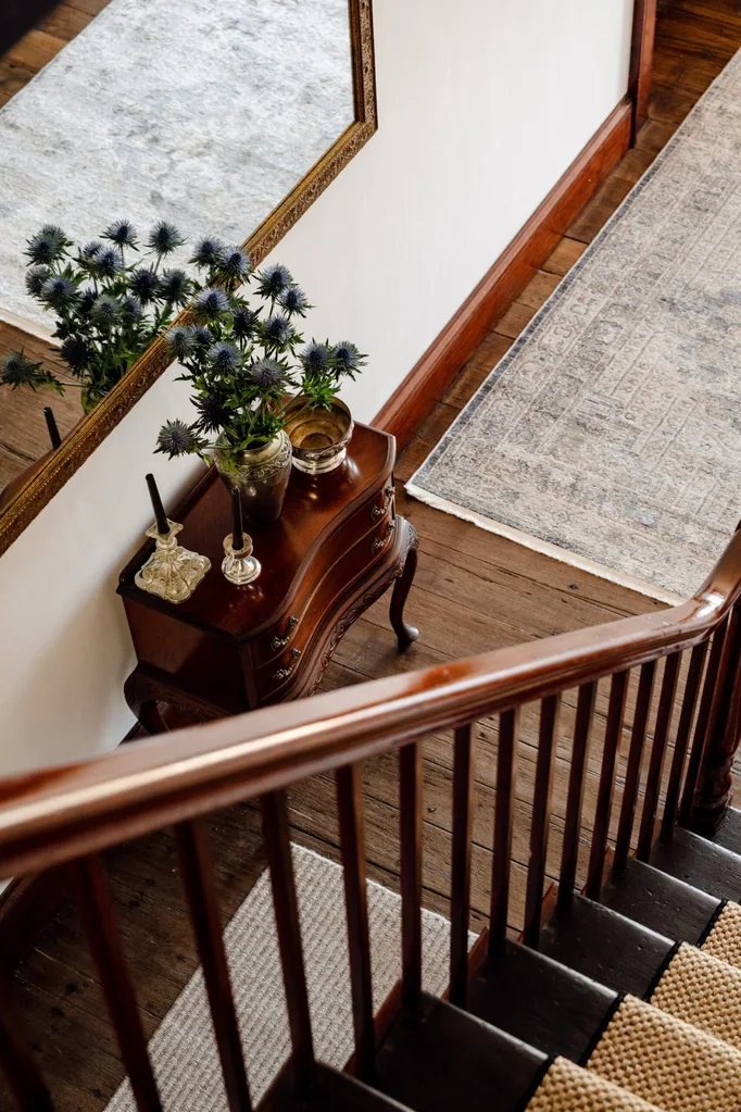 A view down the stairs into an entryway with wooden floorboards and antique furniture.
