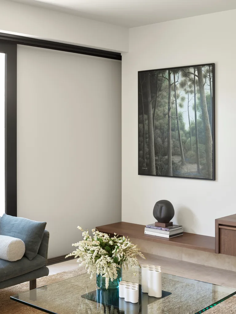 A cosy corner of a living area with white walls, American oak joinery shelving and a large glass coffee table.