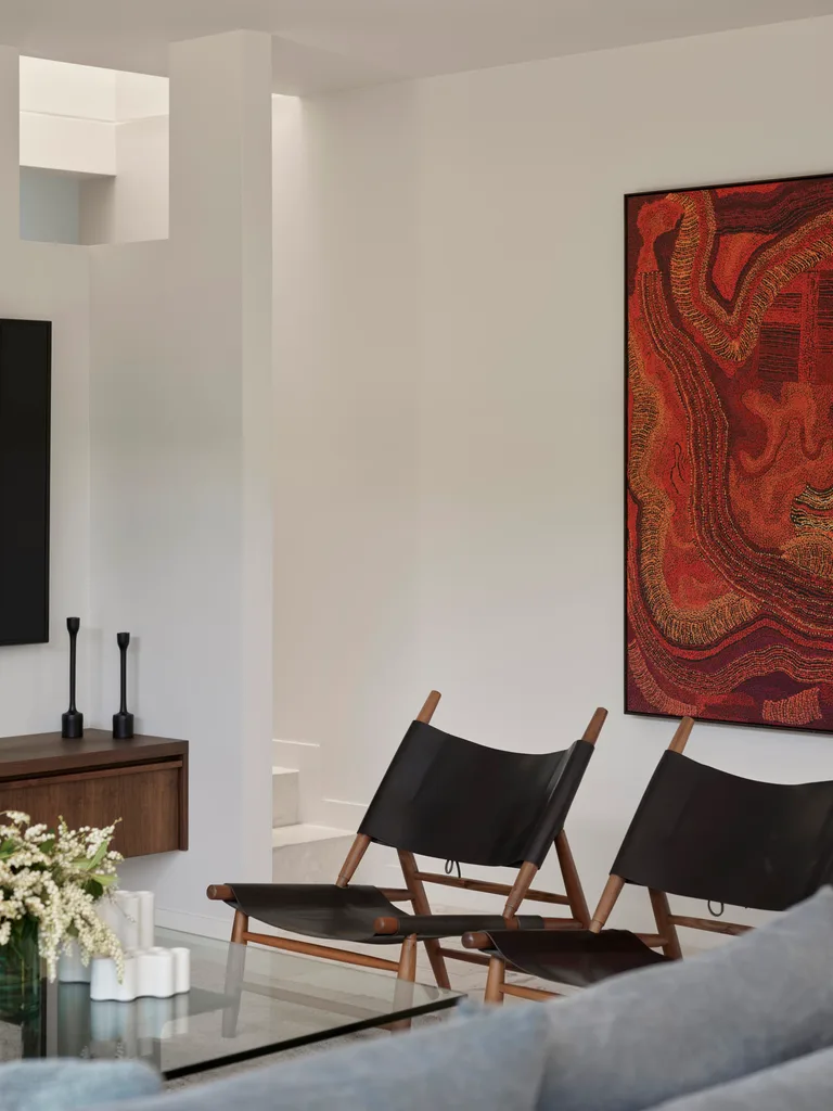 A living area with white walls, black leather and wood chairs and a large, red hued artwork.
