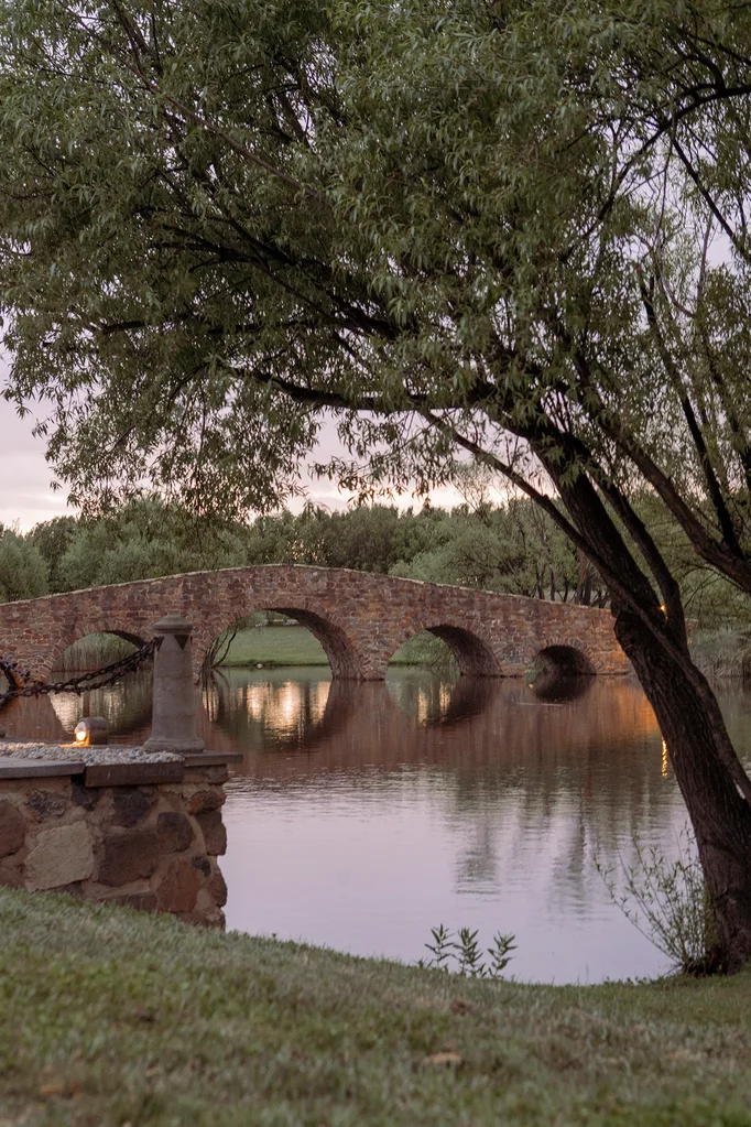 A stone humpbacked bridge arches over a tree-fringed lake.