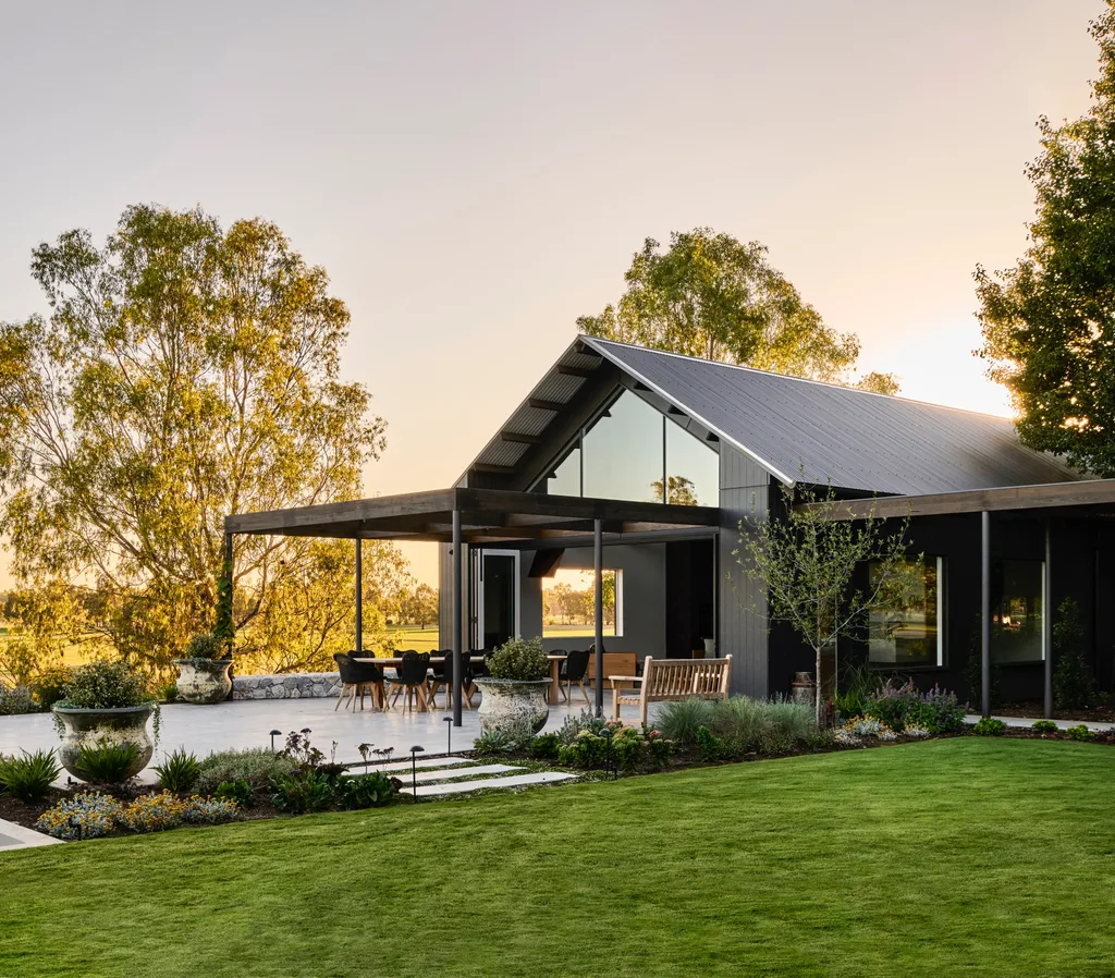 A black-clad barn exterior with a bright green lawn and alfresco dining area.