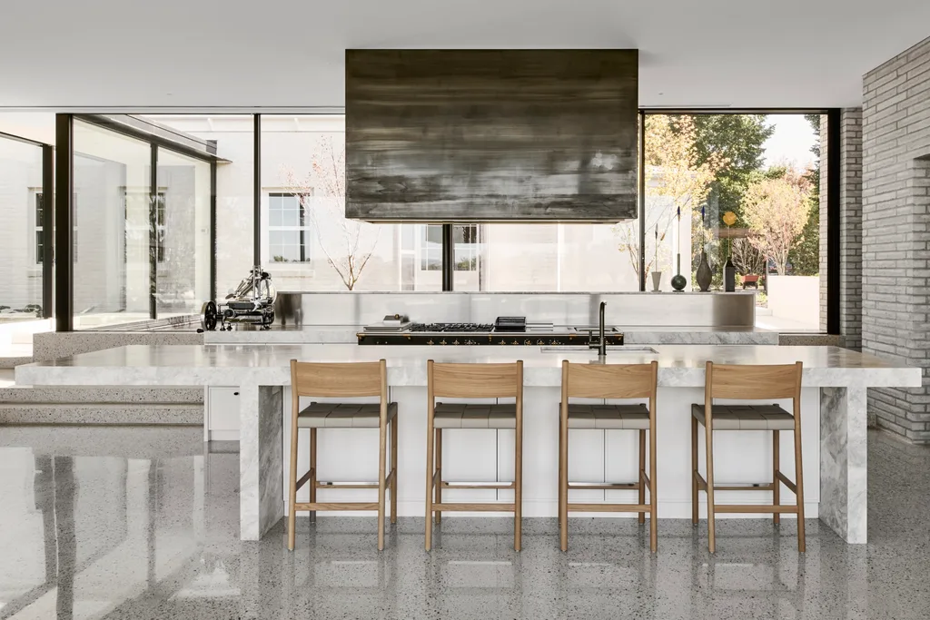 A large, open plan white kitchen with a marble island and dramatic black range hood.