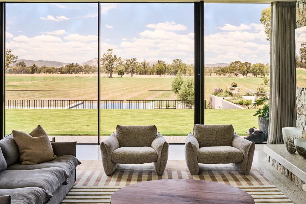 In a luxurious sitting room, floor-to-ceiling windows look out onto a large green lawn and the hilly terrain beyond.