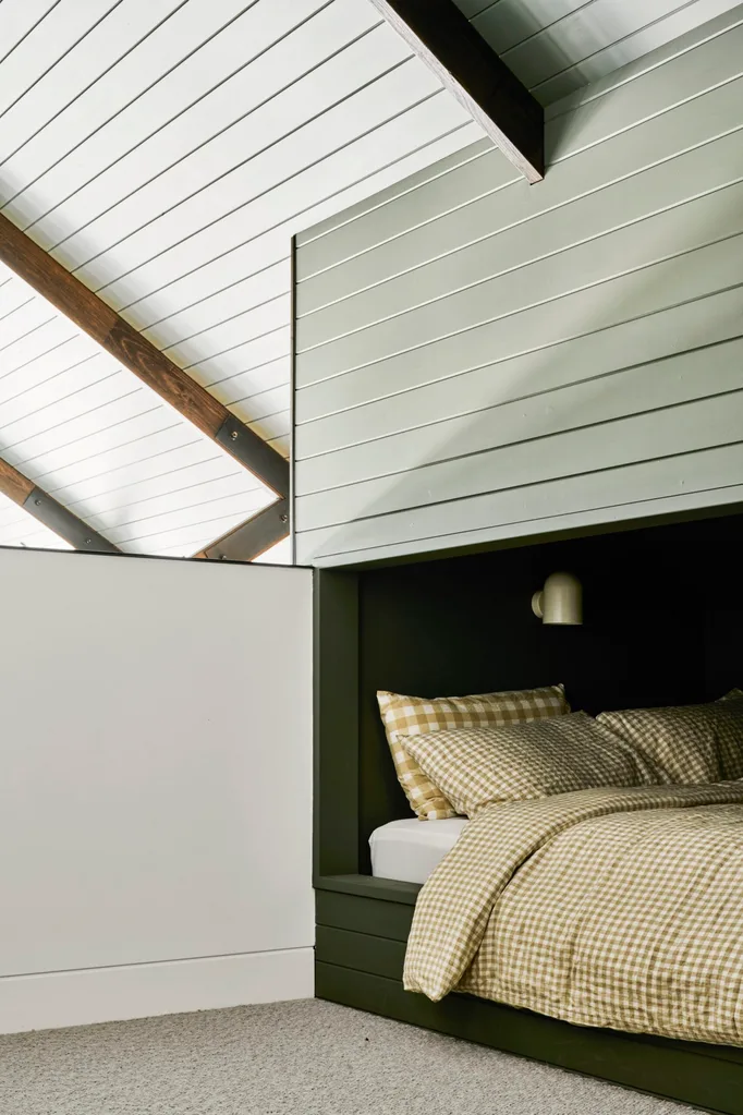On the mezzanine level of a barn-style building, a bed with gingham linen is tucked into a nook.