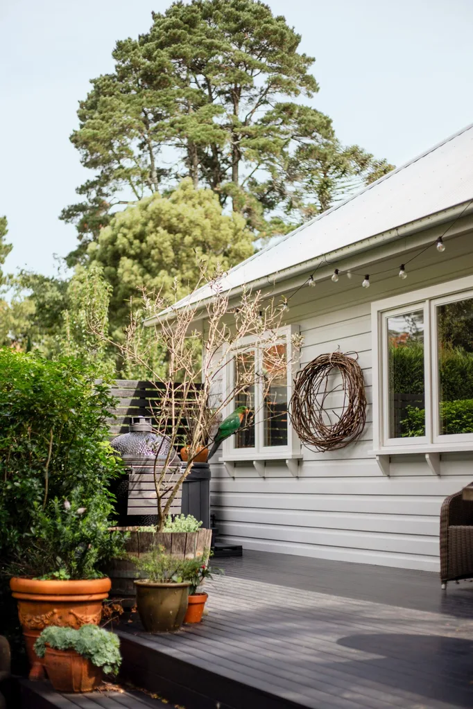 A deck area beside a weatherboard home with pot plants