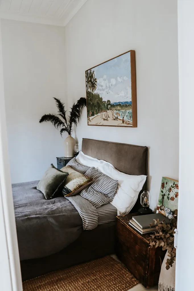 A bedroom with soft grey linen on the bed and a coastal painting hanging above the bed