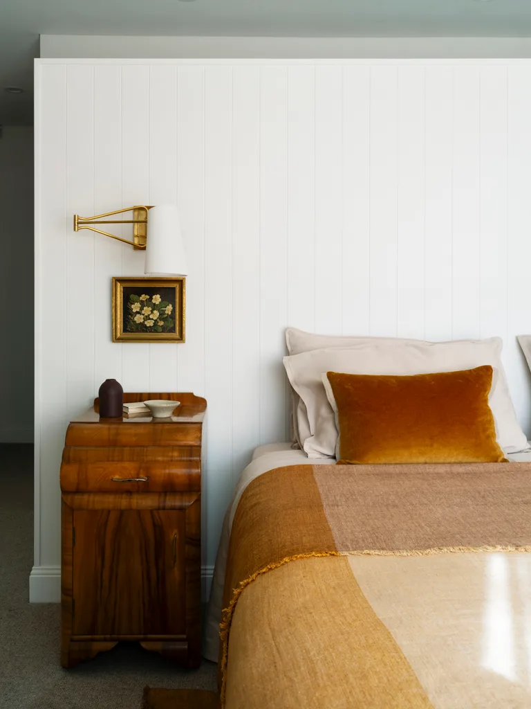 A bedroom with orange bedding, white timber panelling and a wall sconce
