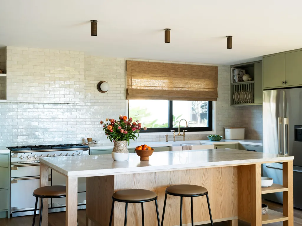 An open-plan kitchen with a timber island bench, subway tiles and green cabinetry