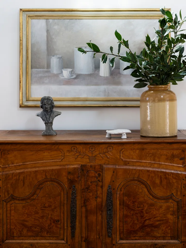 A vintage timber cabinet topped with a sculpture and vase