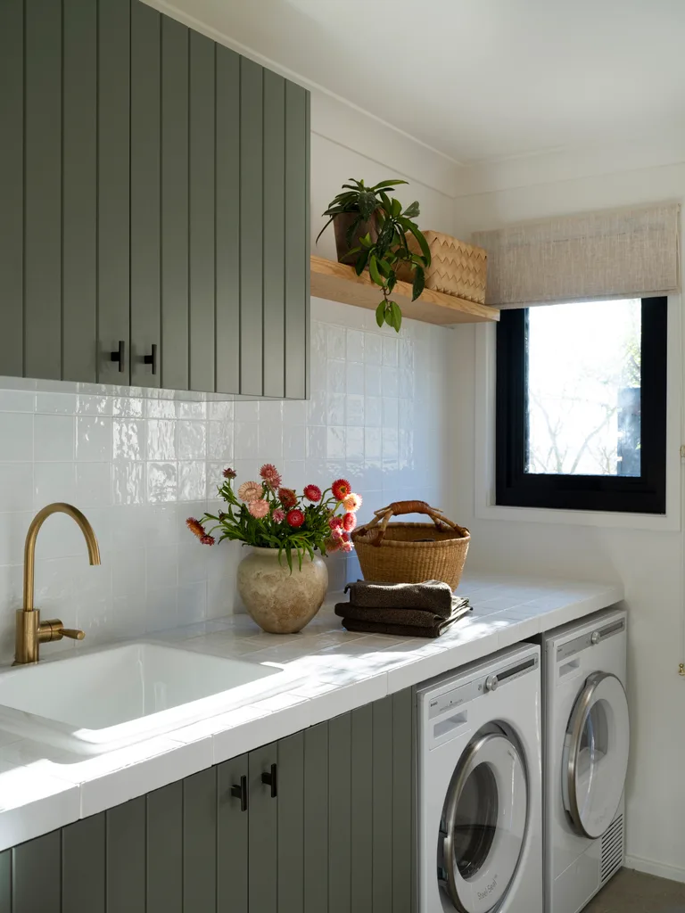 A laundry with green cabinetry and a white splashback