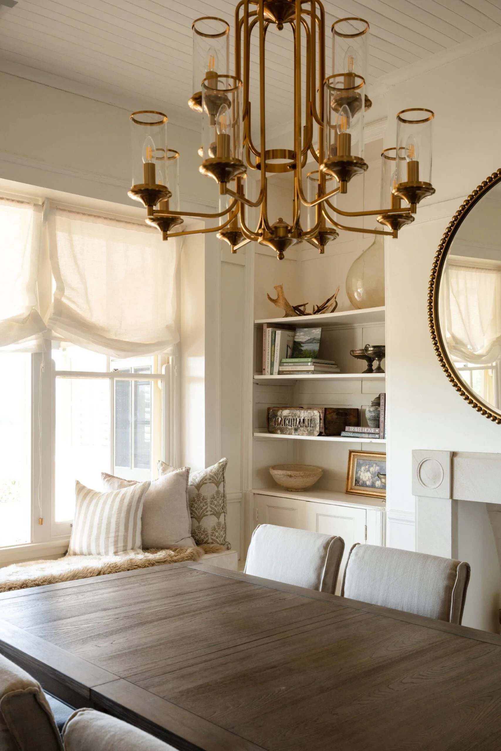 A light-filled dining area with a brass chandelier and window seat