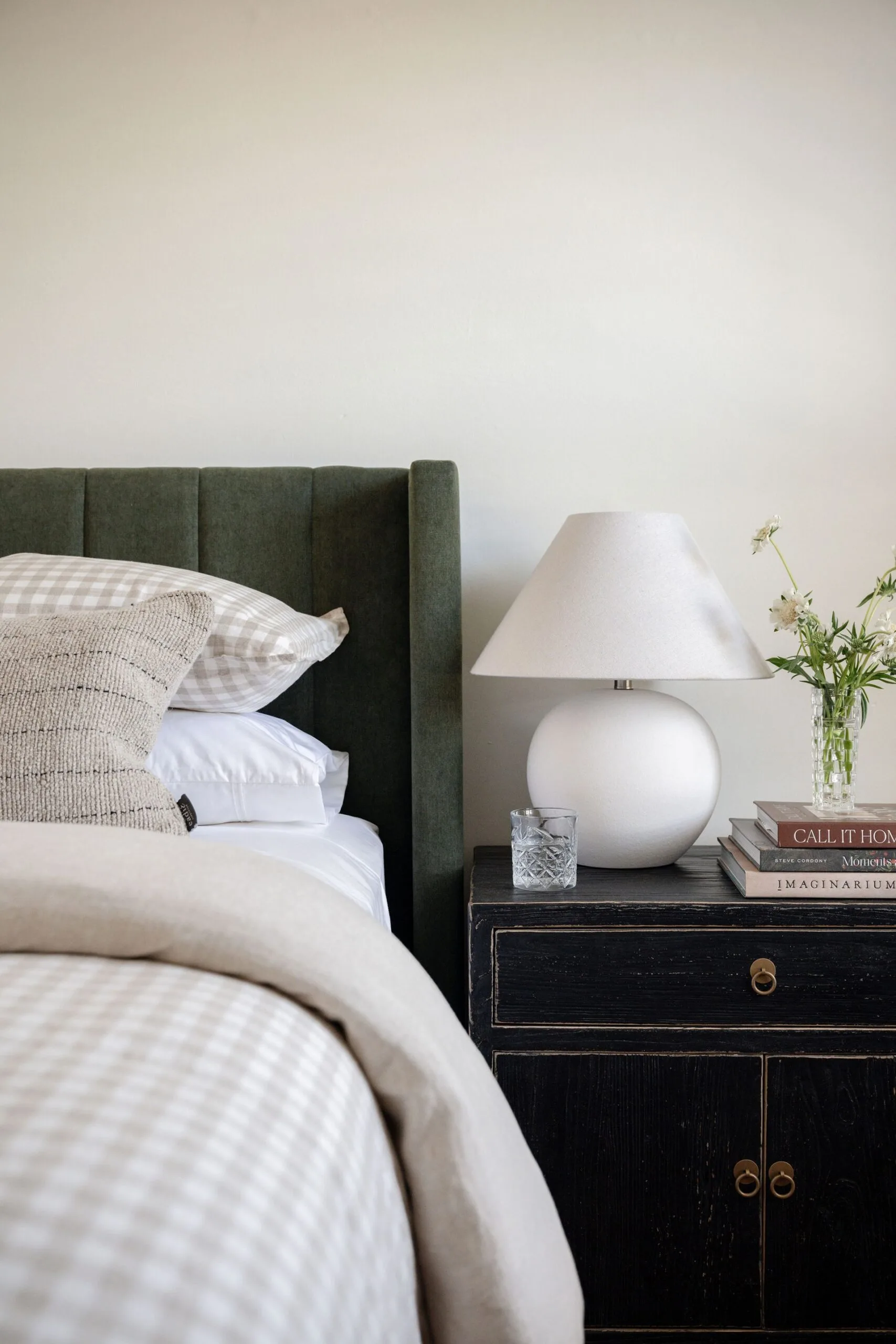 A stylish bedroom with a green headboard and antique-style bedside table