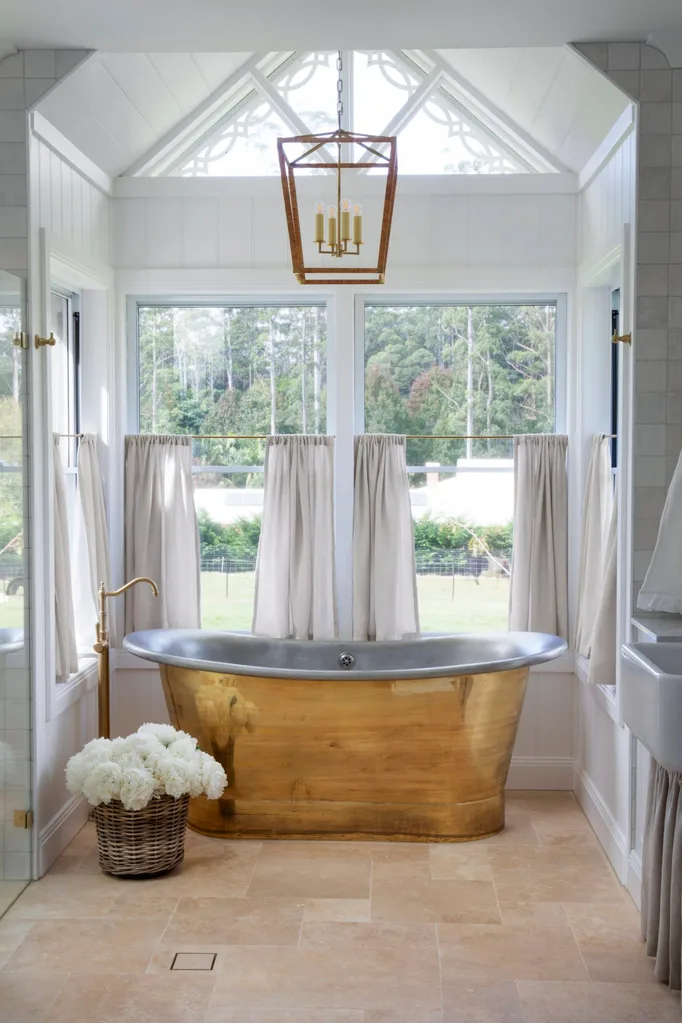 Farmhouse bathroom with a brass and tin bath, brass tapware, large windows, and linen curtains