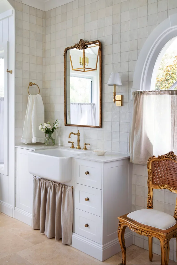 Neutral bathroom with zellige tiles, an antique mirror and chair, and a farmhouse sink