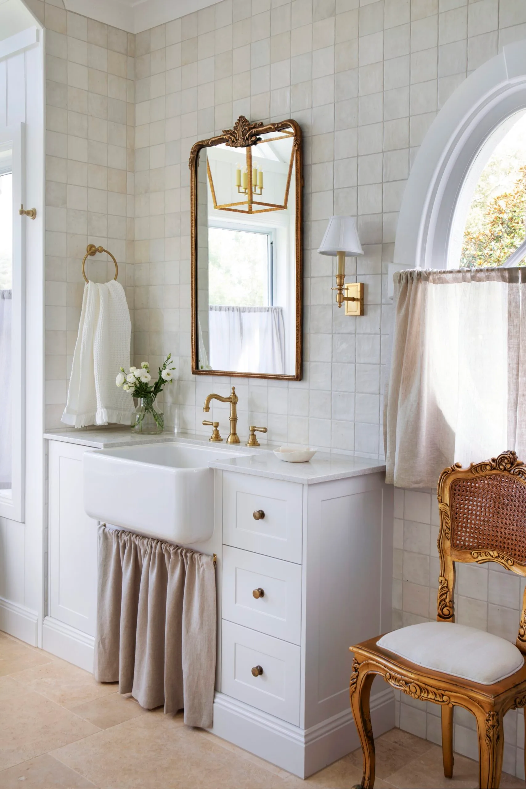 Neutral bathroom with zellige tiles, an antique mirror and chair, and a farmhouse sink