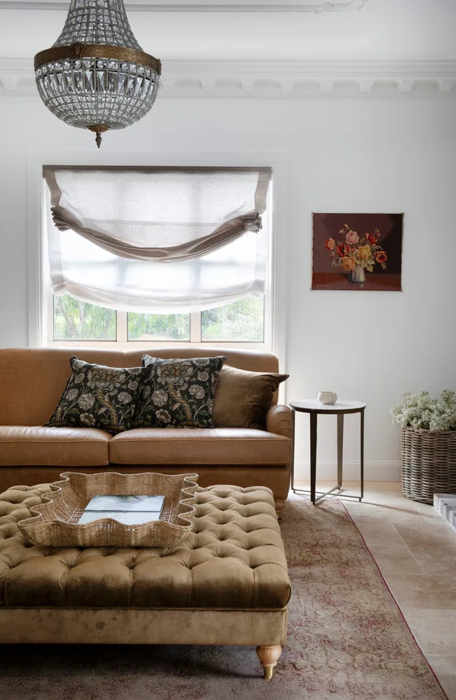 Living room with a brown ottoman and sofa, tapestry, an Art Deco chandelier, and linen curtains