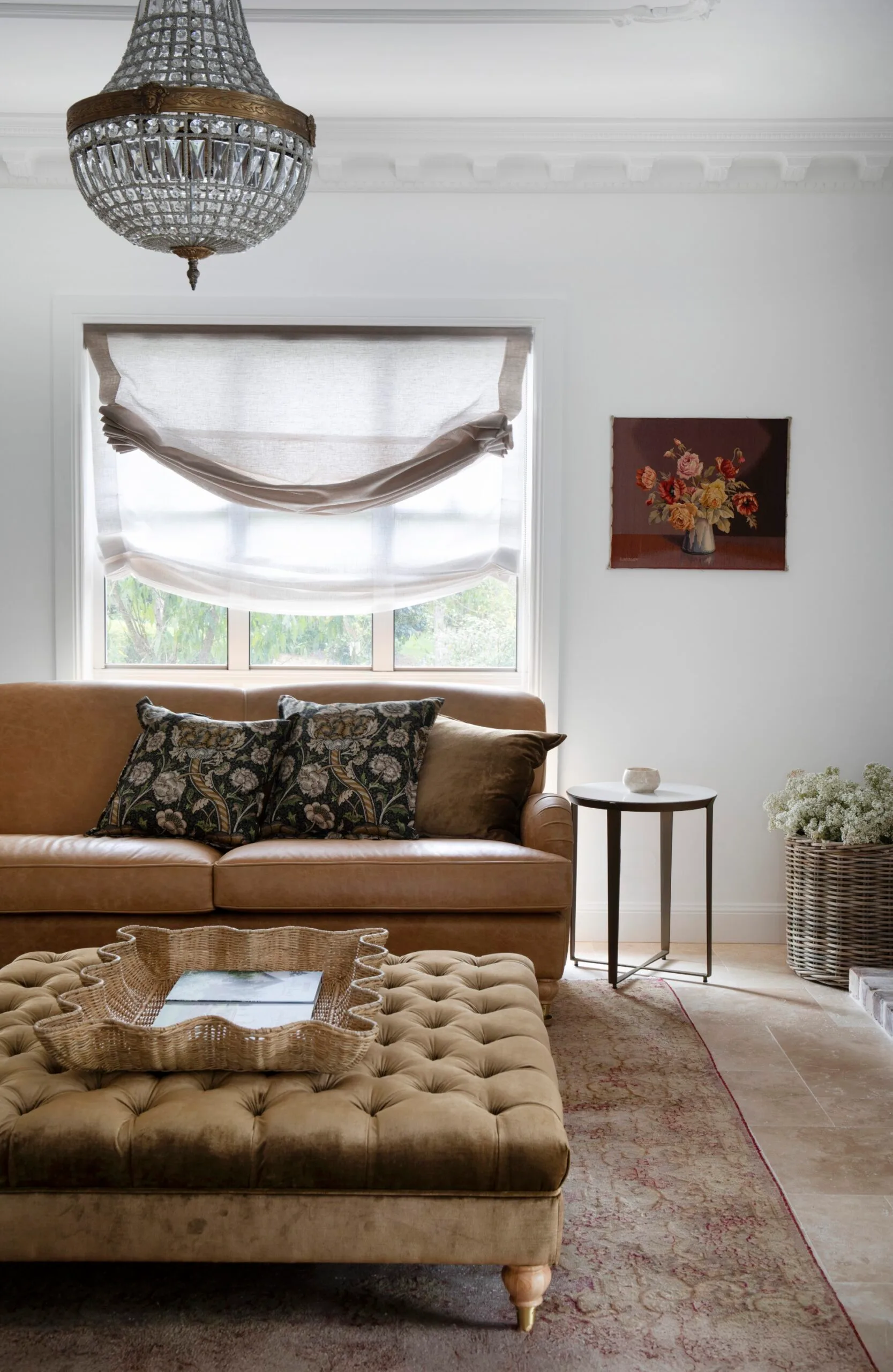 Living room with a brown ottoman and sofa, tapestry, an Art Deco chandelier, and linen curtains