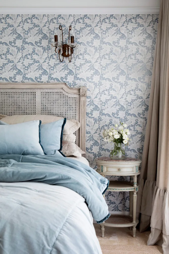 Guest bedroom with floral blue Morris & Co wallpaper, a rattan bedhead, and blue linen