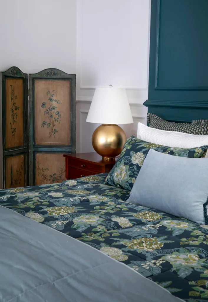 Teal panelled bedhead, vintage screen, brass lamp, and floral linen