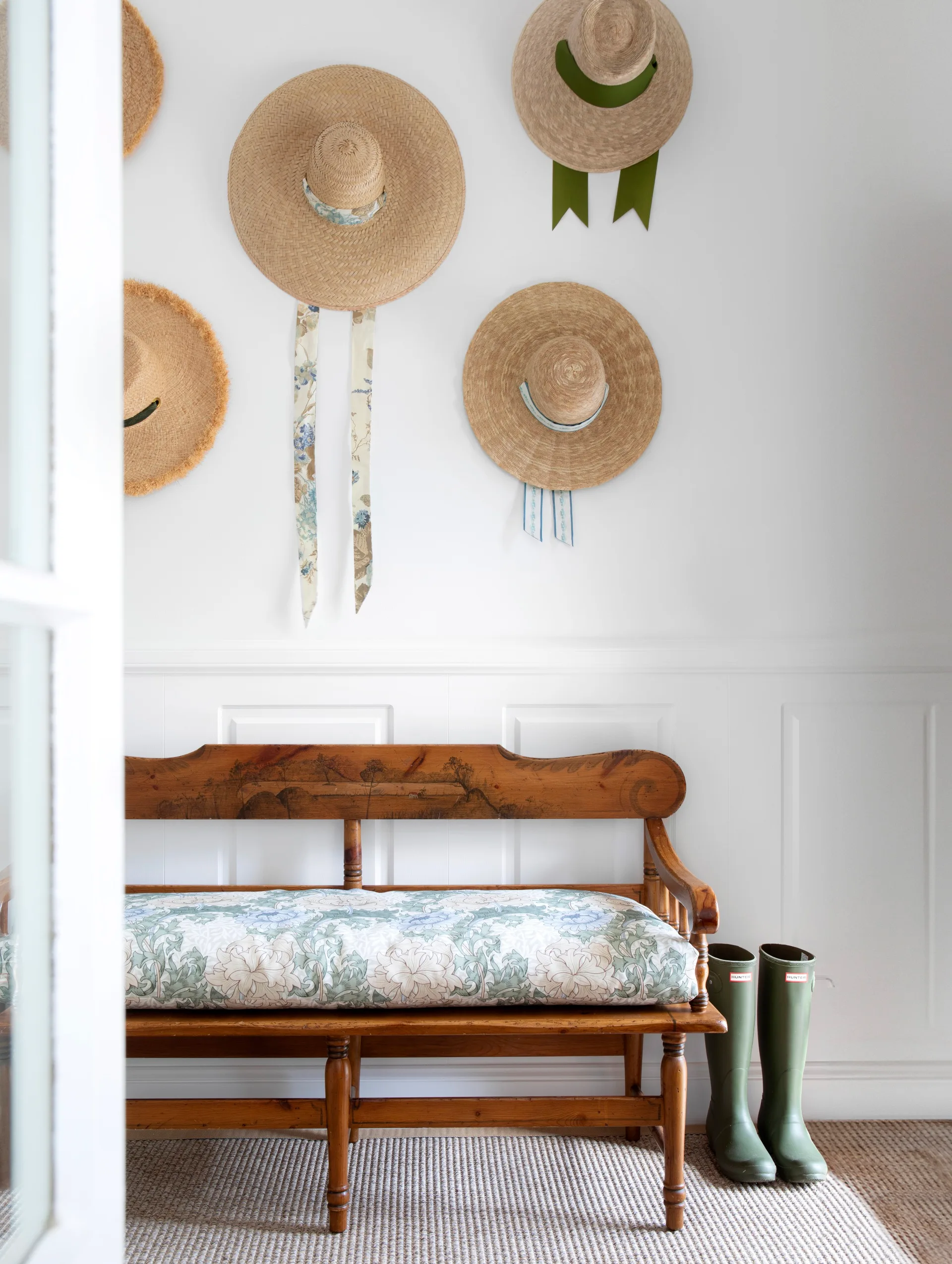 Hallway or entry with white wainscoting, a vintage bench seat, and a display of hats on the wall
