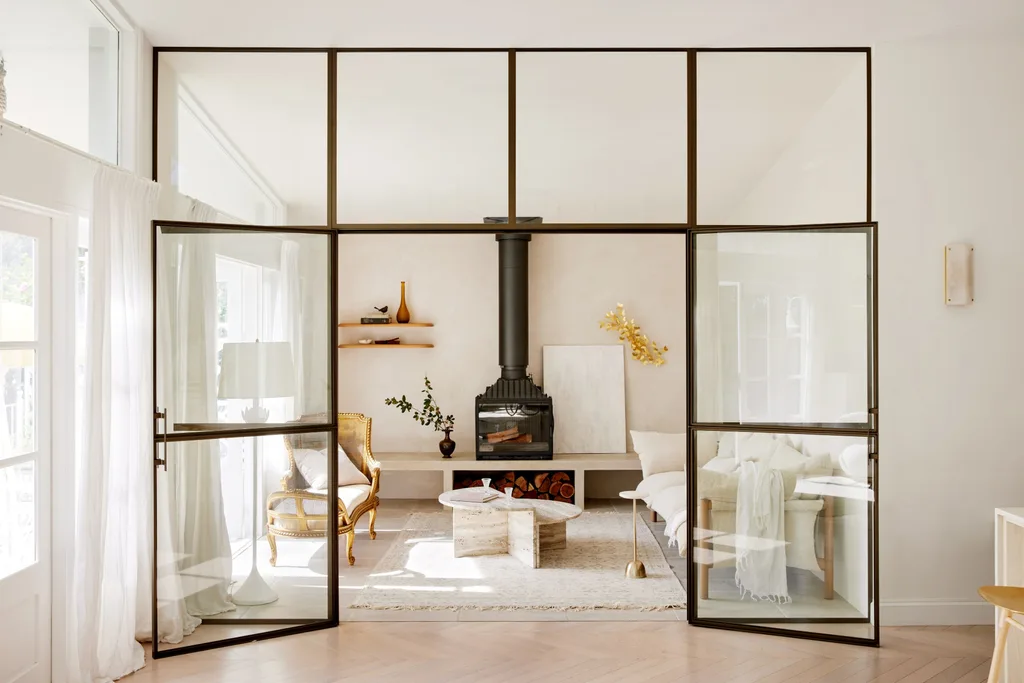White living room featuring interior steel doors, a travertine coffee table, wood fire, and a rattan daybed.