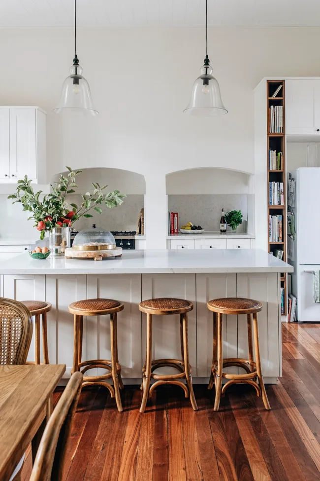 A modern country kitchen with a white island bench and timber bar stools