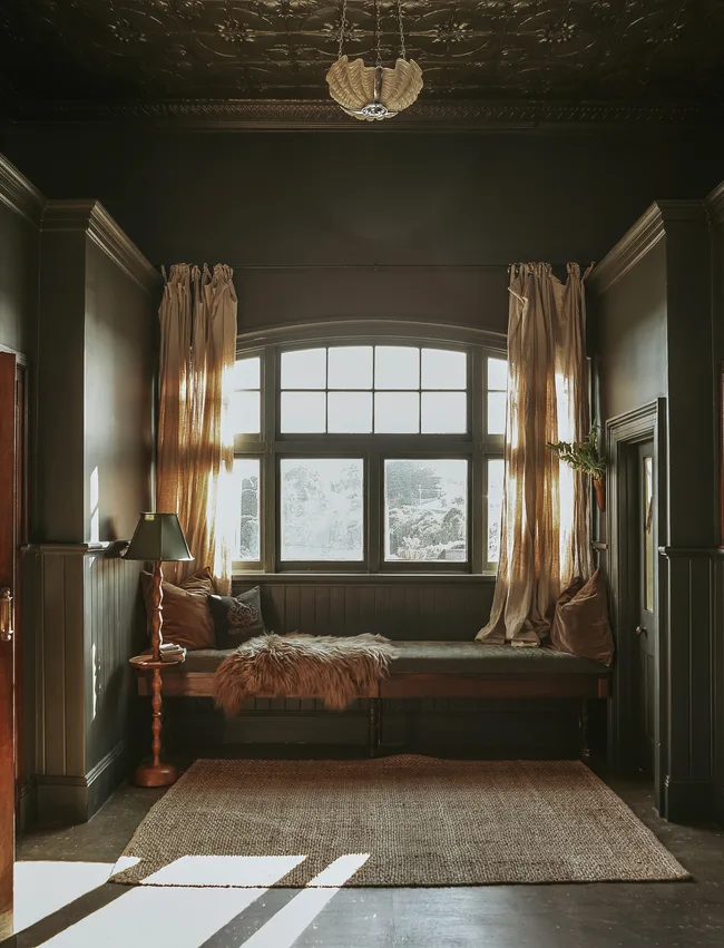 A cosy green window seat beneath pressed metal ceilings