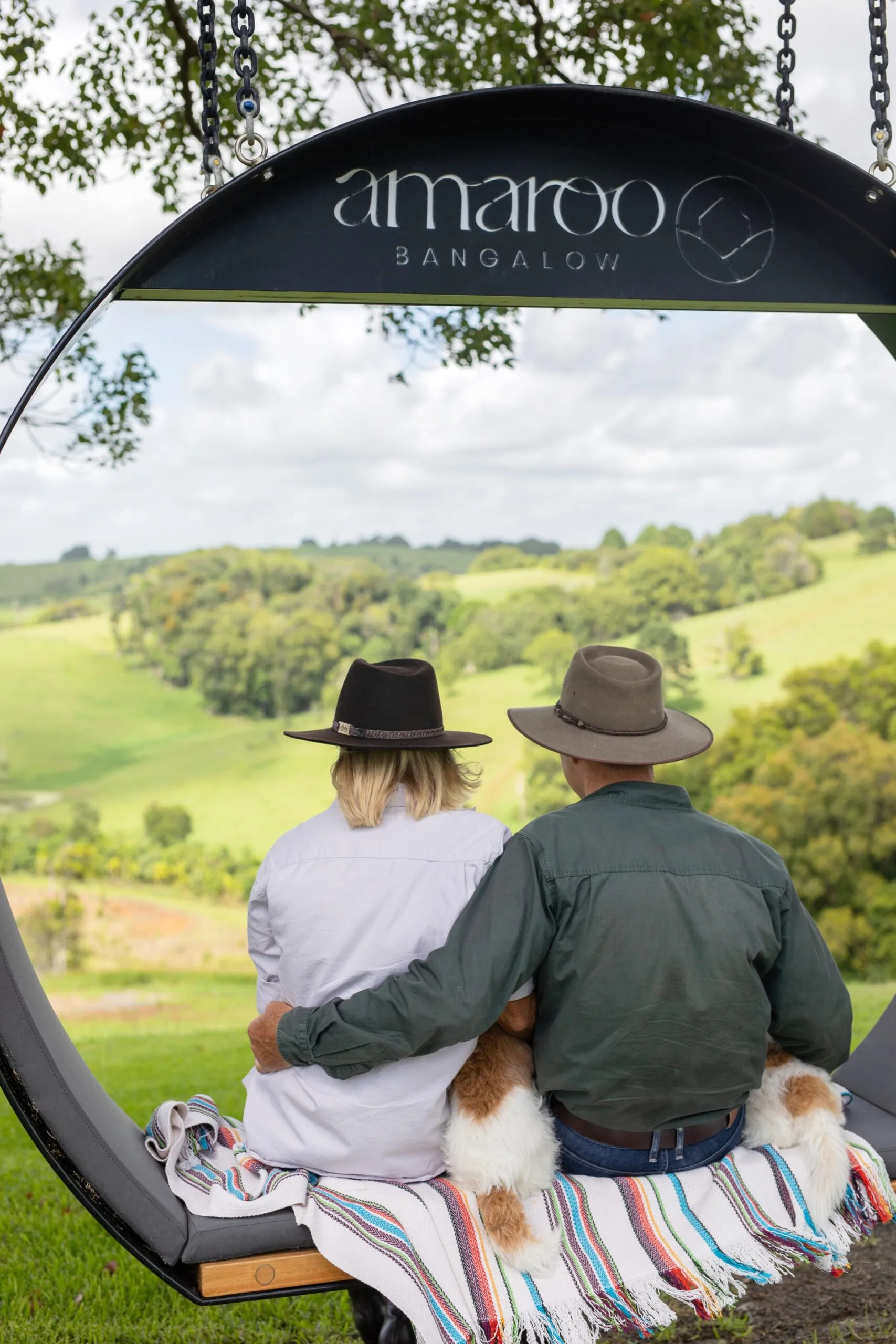 A couple sat on a swing with two dogs overlooking the hinterland