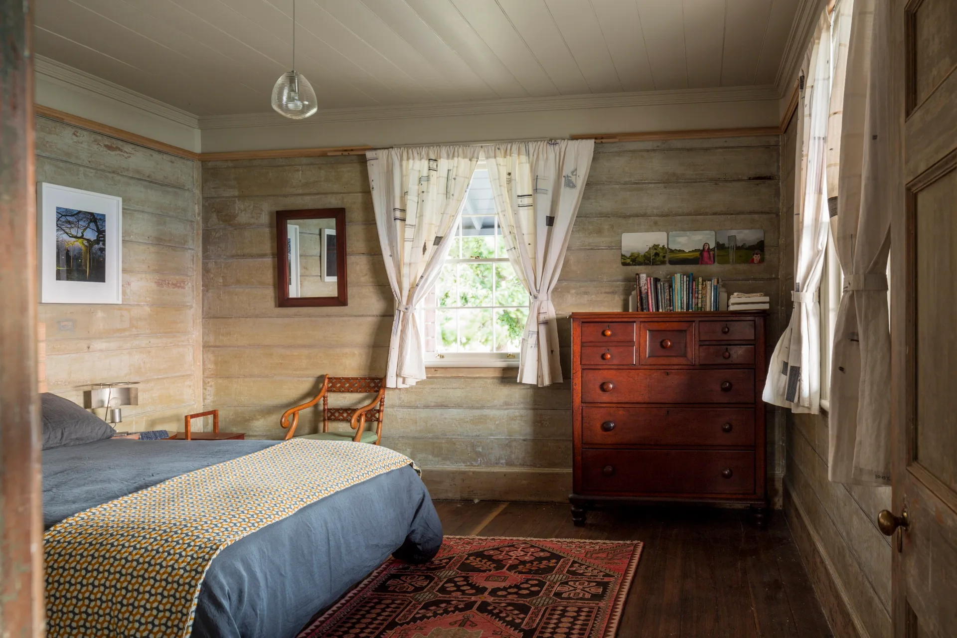 A bedroom within Captain Kelly's Cottage with rustic timber panelling and sash windows