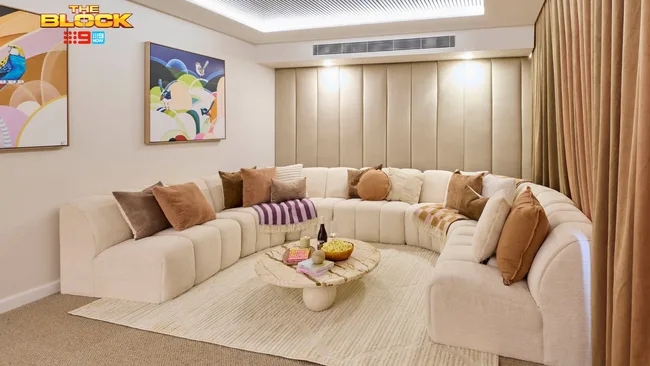 A curved cream boucle sofa sits in the back end of a neutral coloured rumpus room.