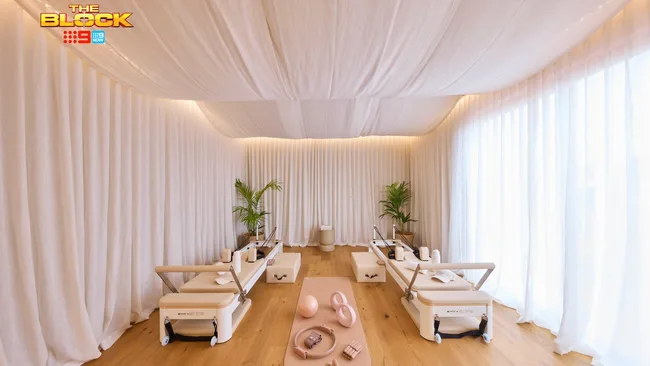 A soft blush-coloured Pilates studio with two reformer beds and equipment, featuring draped fabric walls and ceiling. The Block Britt and Taz