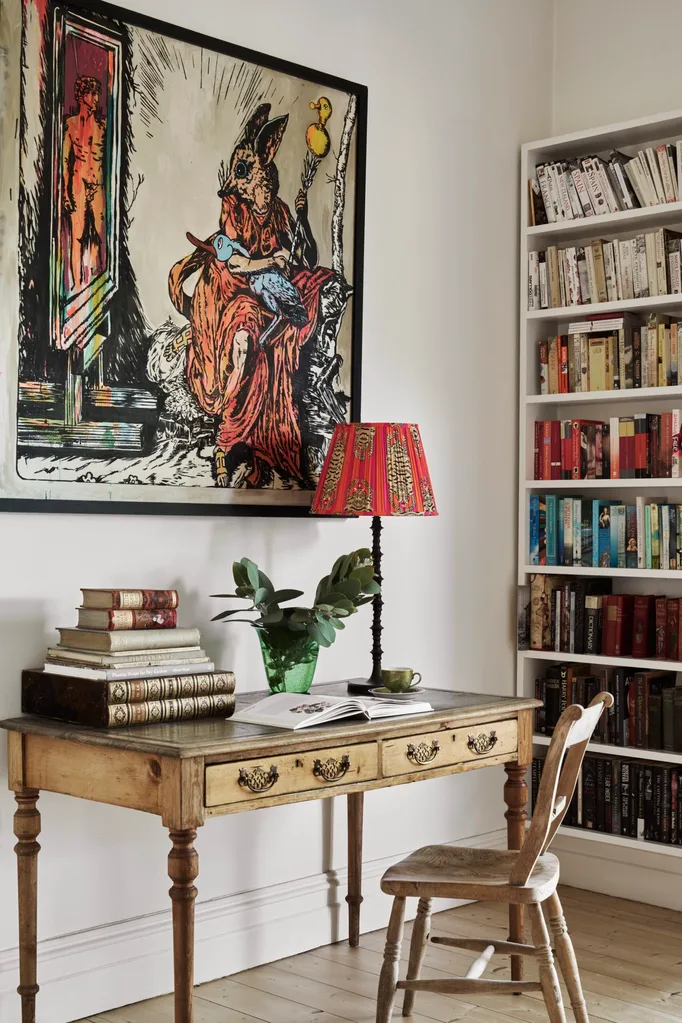 A quaint writer's desk with a framed art work above and a white bookshelf